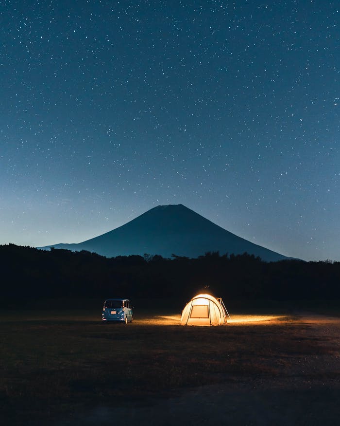 A serene camping setup under a starry sky with Mount Fuji in the background.